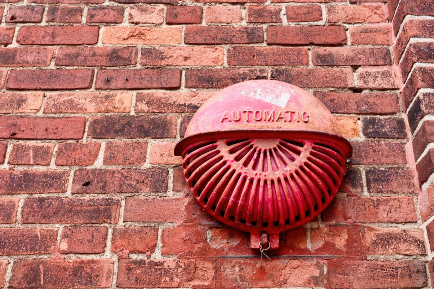 Weathered cast-metal fire alarm bell stamped AUTOMATIC on an aged red brick wall