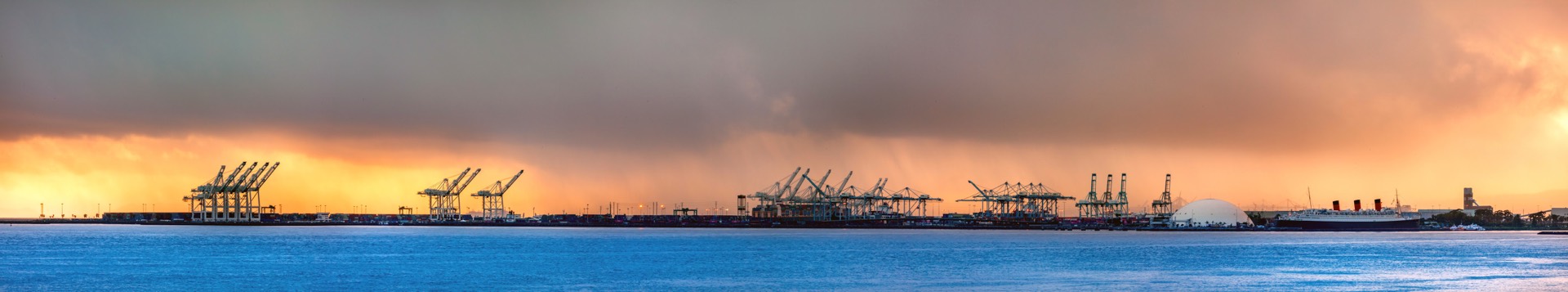 Panorama of the Port of Long Beach at stormy sunset with container cranes and the Queen Mary