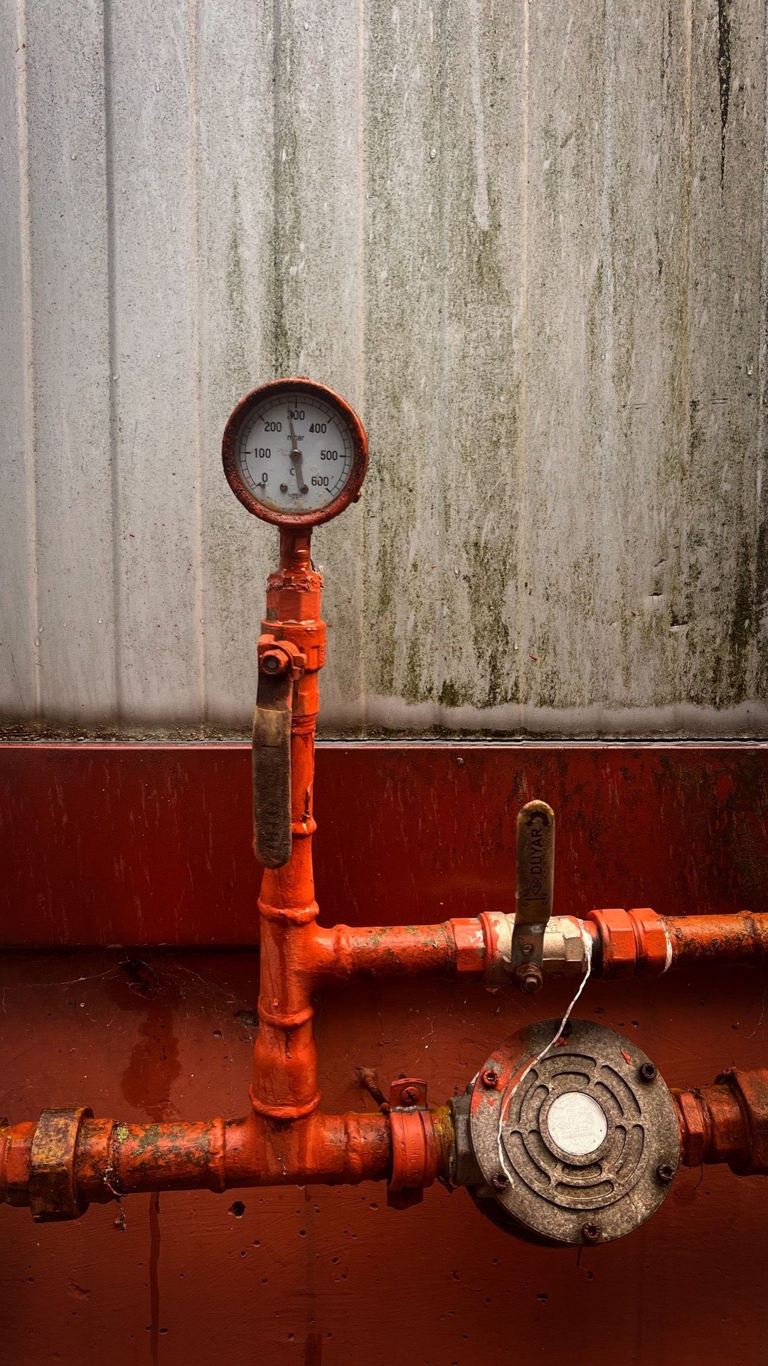 Weathered pressure gauge, valve and water-motor alarm gong on red fire sprinkler piping