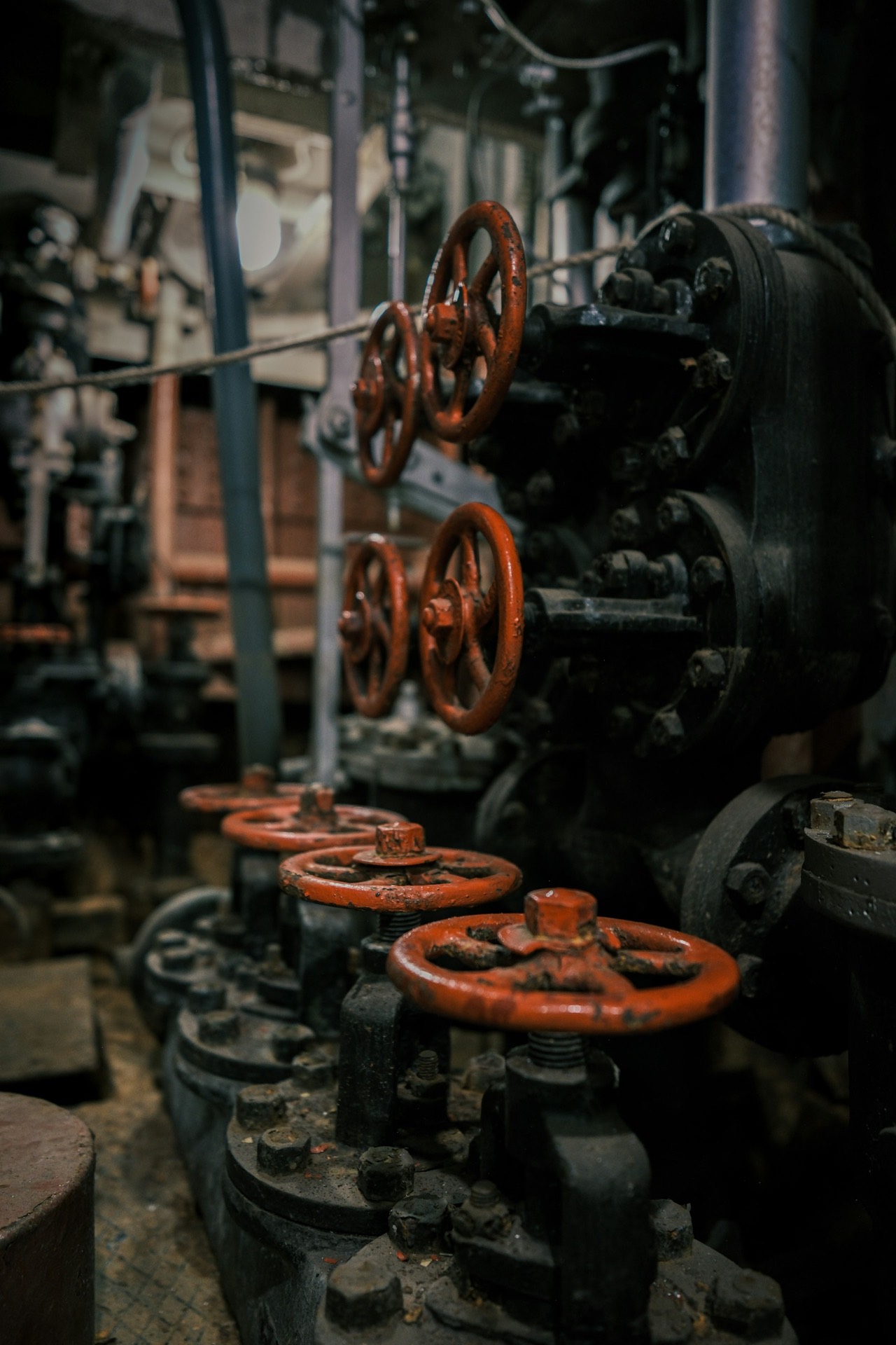 Receding row of red valve handwheels on dark cast-iron machinery in a vintage plant room