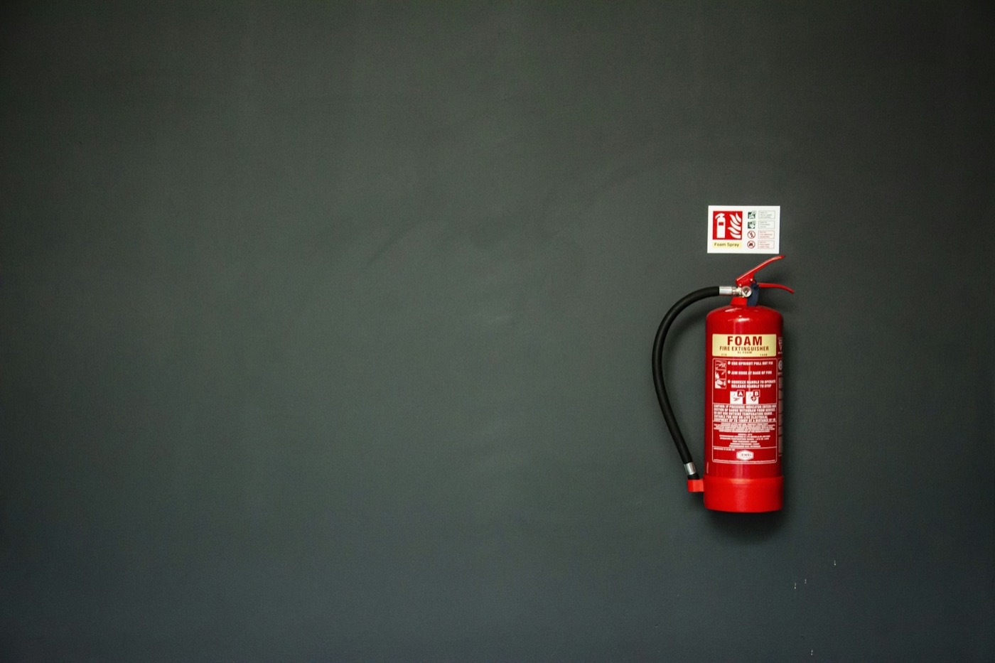 Red fire extinguisher mounted on a dark charcoal wall with wide empty space beside it