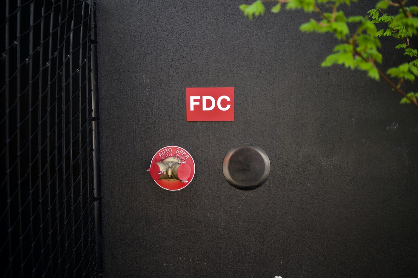 Brass siamese fire department connection and red FDC sign on a near-black building wall