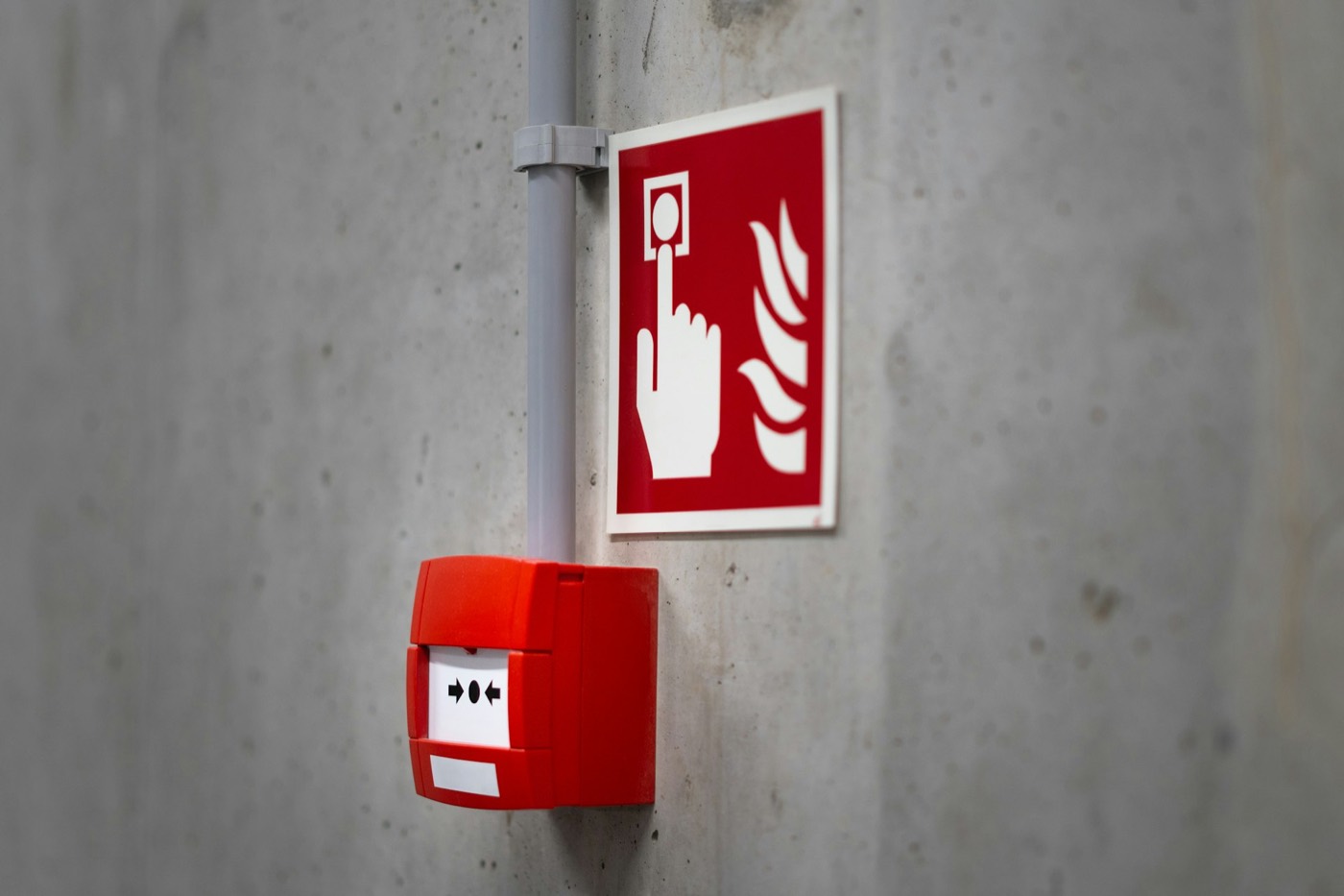 Red manual fire alarm call point and alarm signage mounted on a bare concrete wall