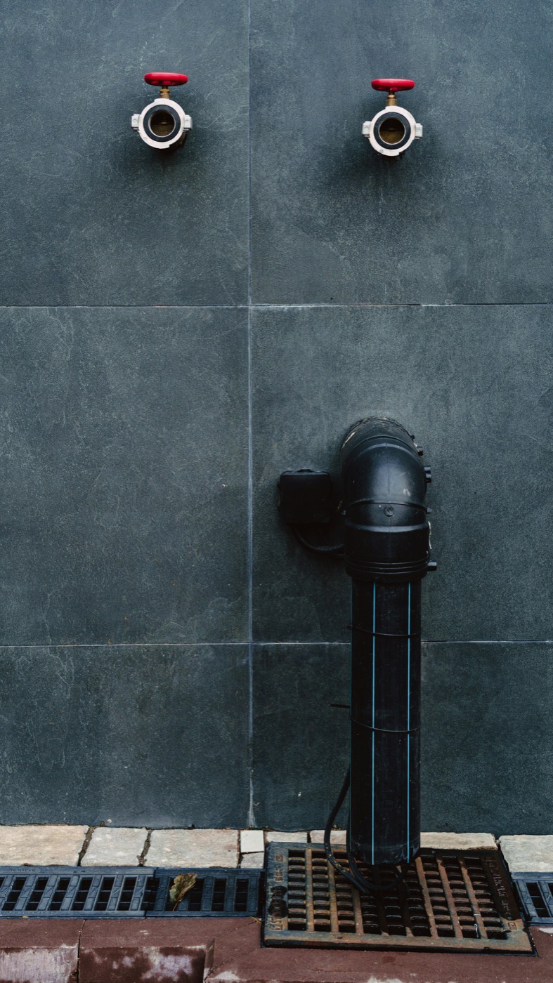 Two wall-mounted hose outlet valves with red handles and chrome couplings on a dark slate wall